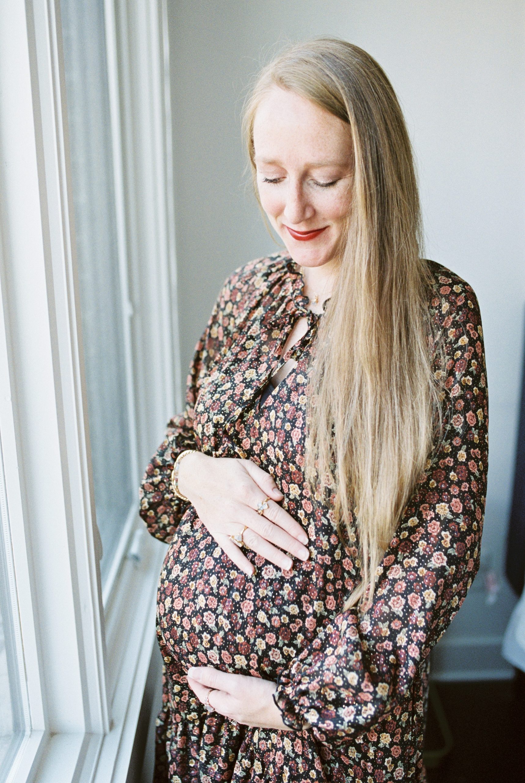 expectant mom standing next to window posing for maternity photos