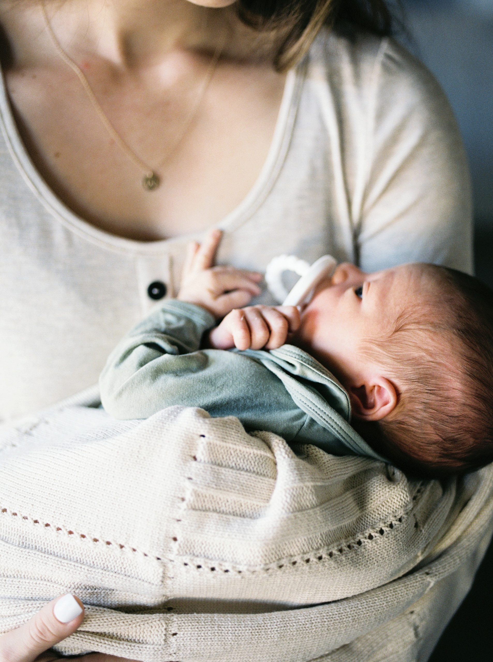 mom holds baby boy with pacifier during In Home Lifestyle Newborn portraits