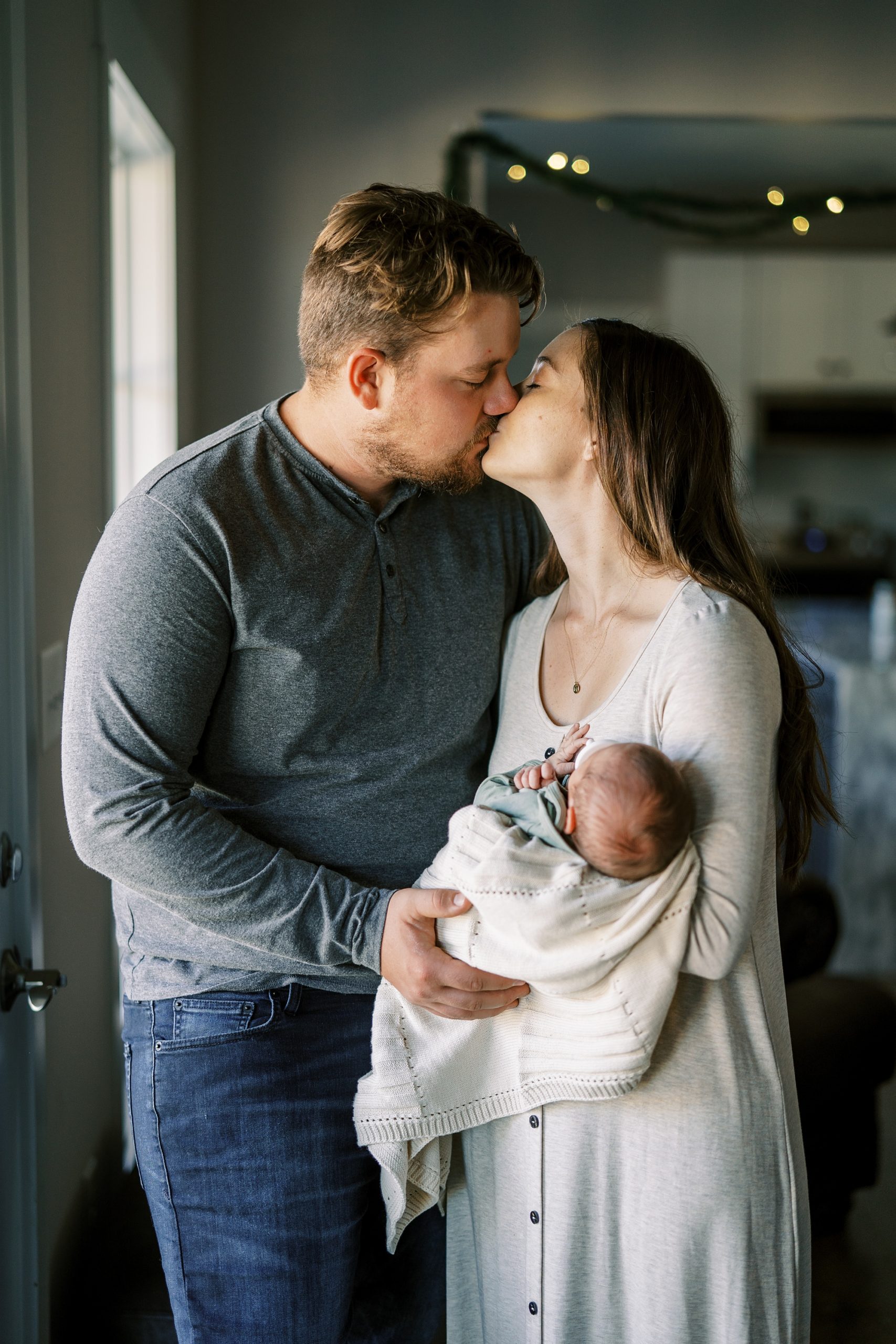 parents kiss while holding newborn baby boy at home