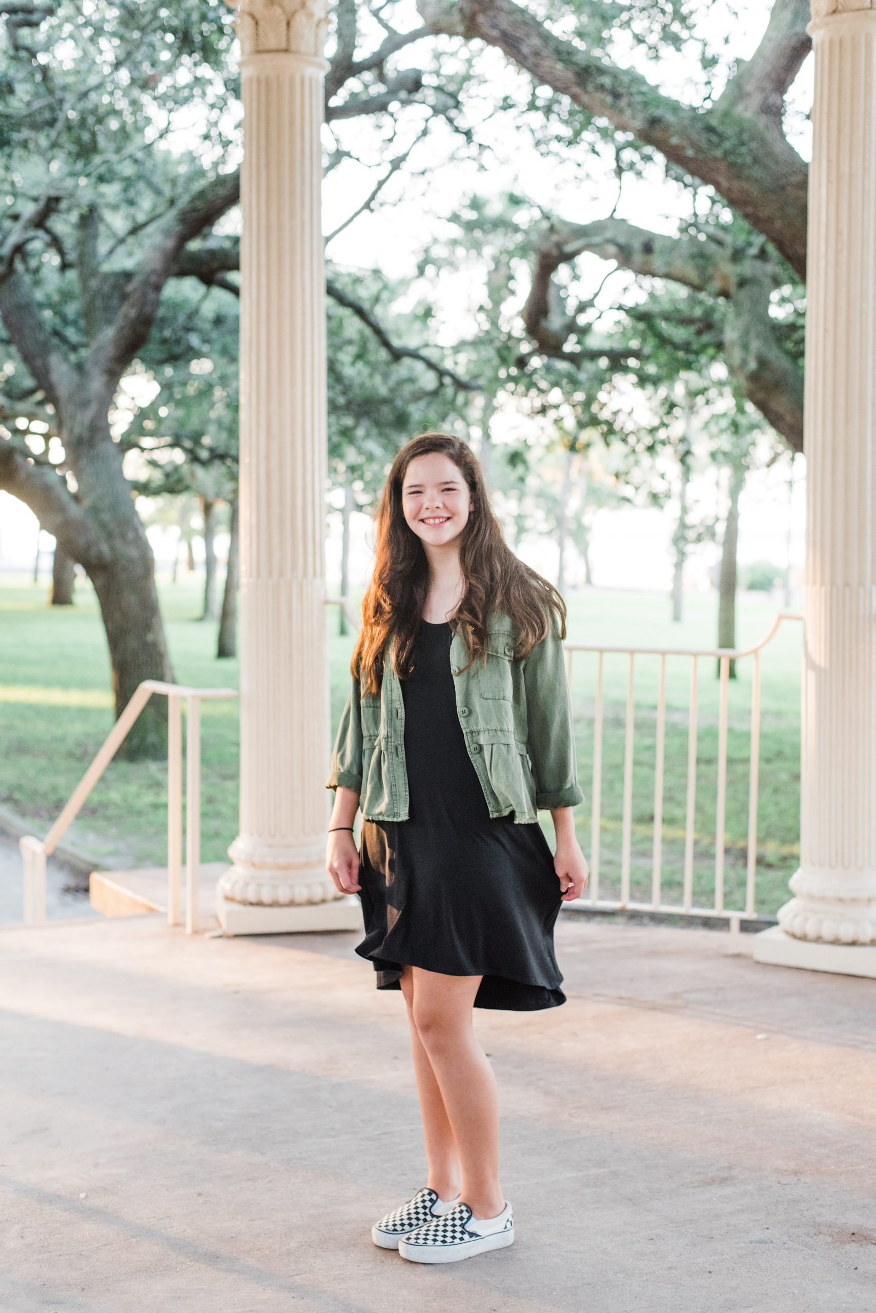 young girl in black dress with green jacket poses in Charleston gazebo
