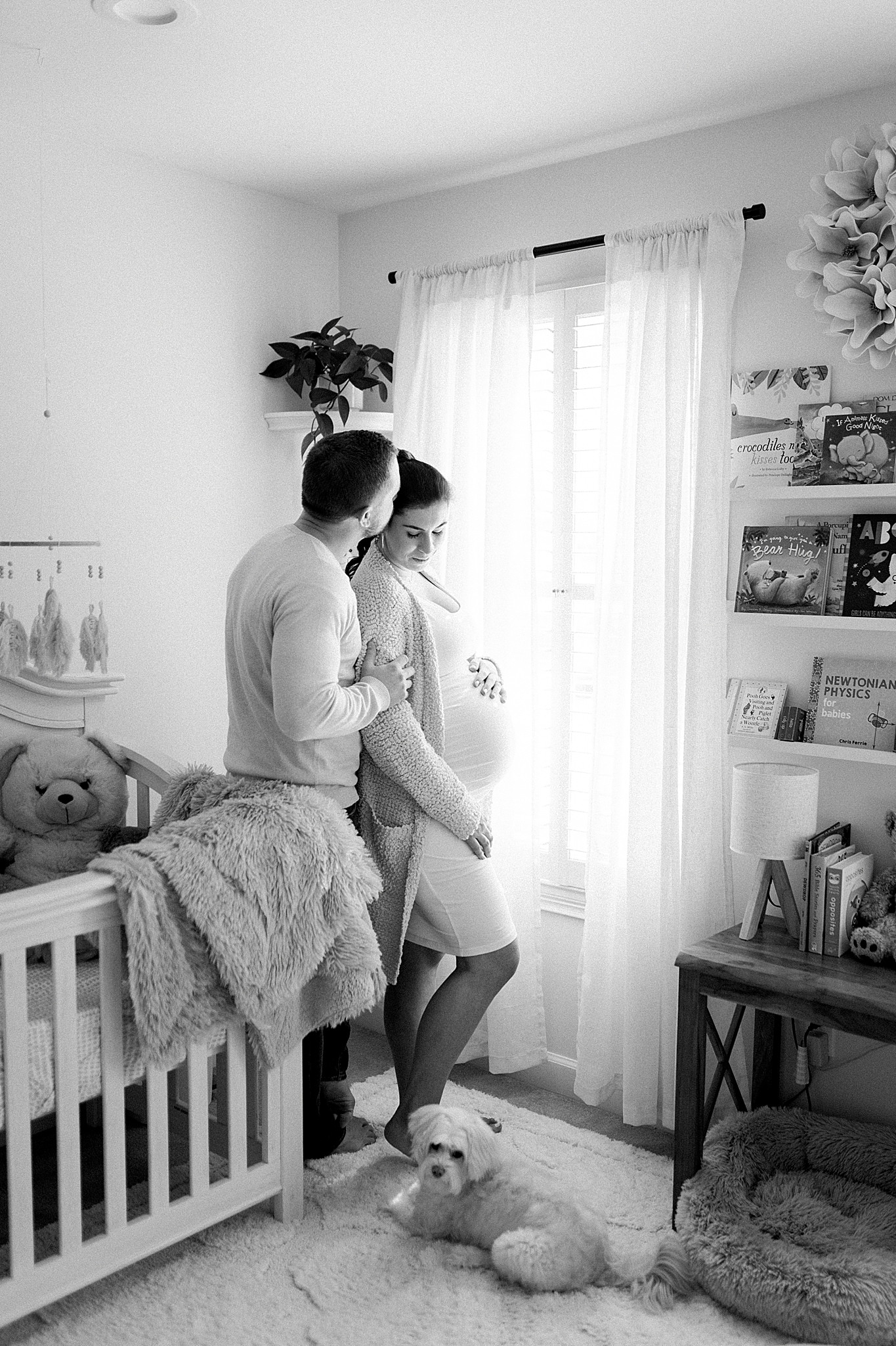 couple poses in daughter's nursery while holding baby belly