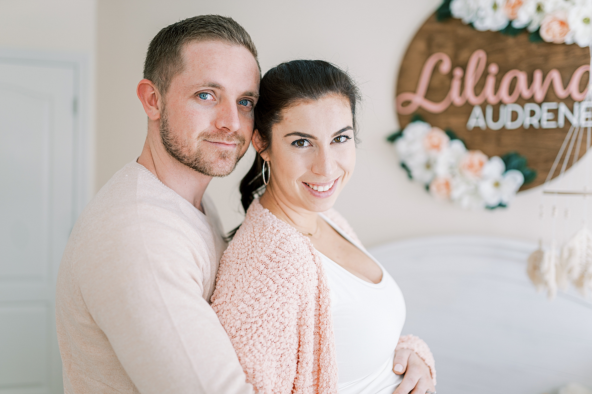 couple poses by wooden sign in nursery during Murfreesboro lifestyle maternity session
