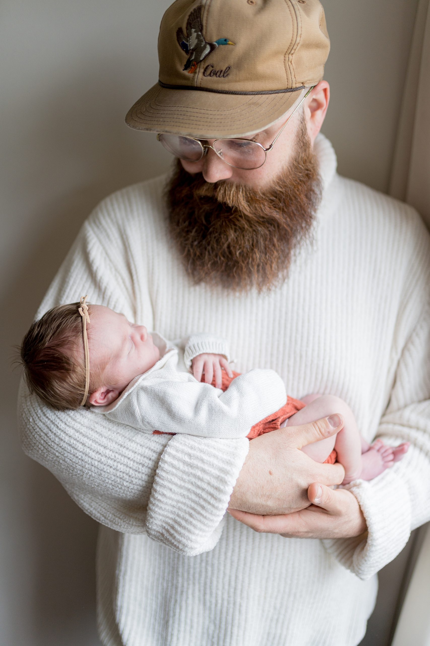 dad holds new daughter and looks down at her during newborn photos