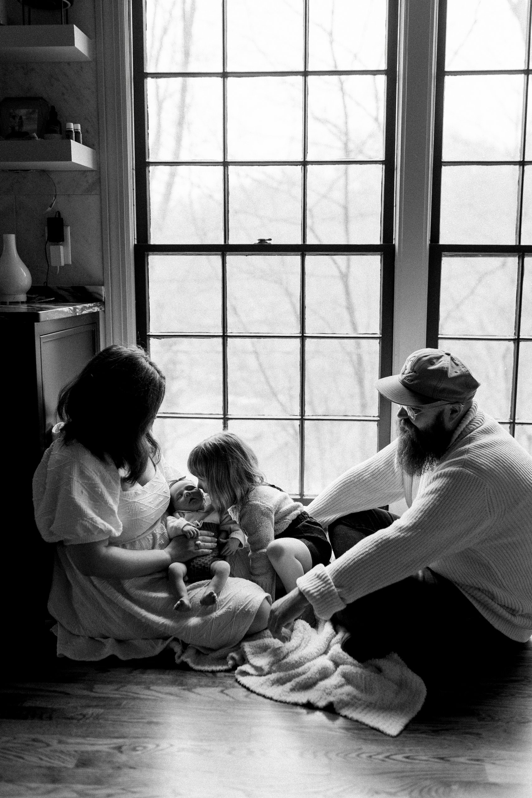 family sits on kitchen floor during newborn photos at home