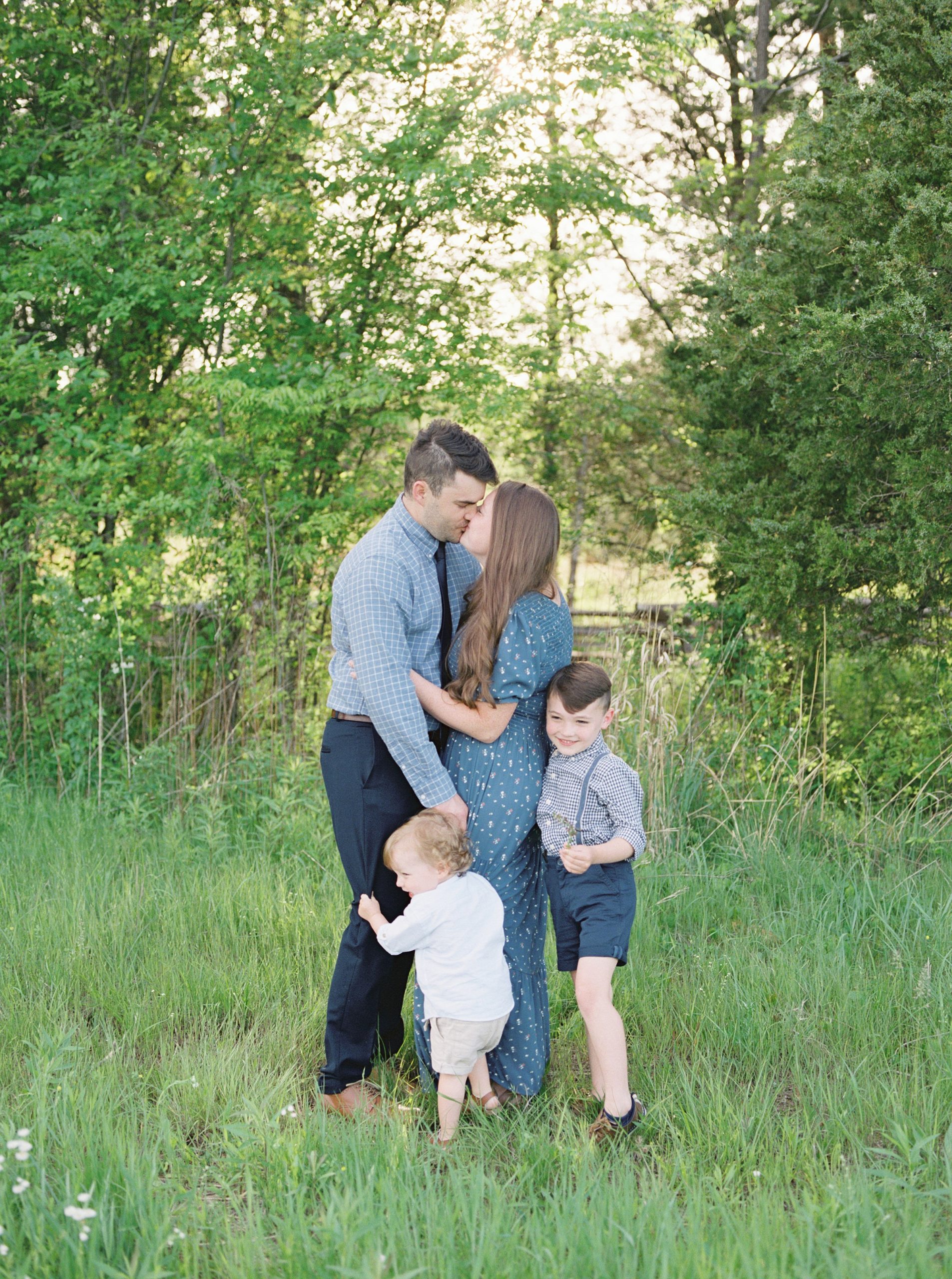 mom and dad kiss while sons hug them during family portraits