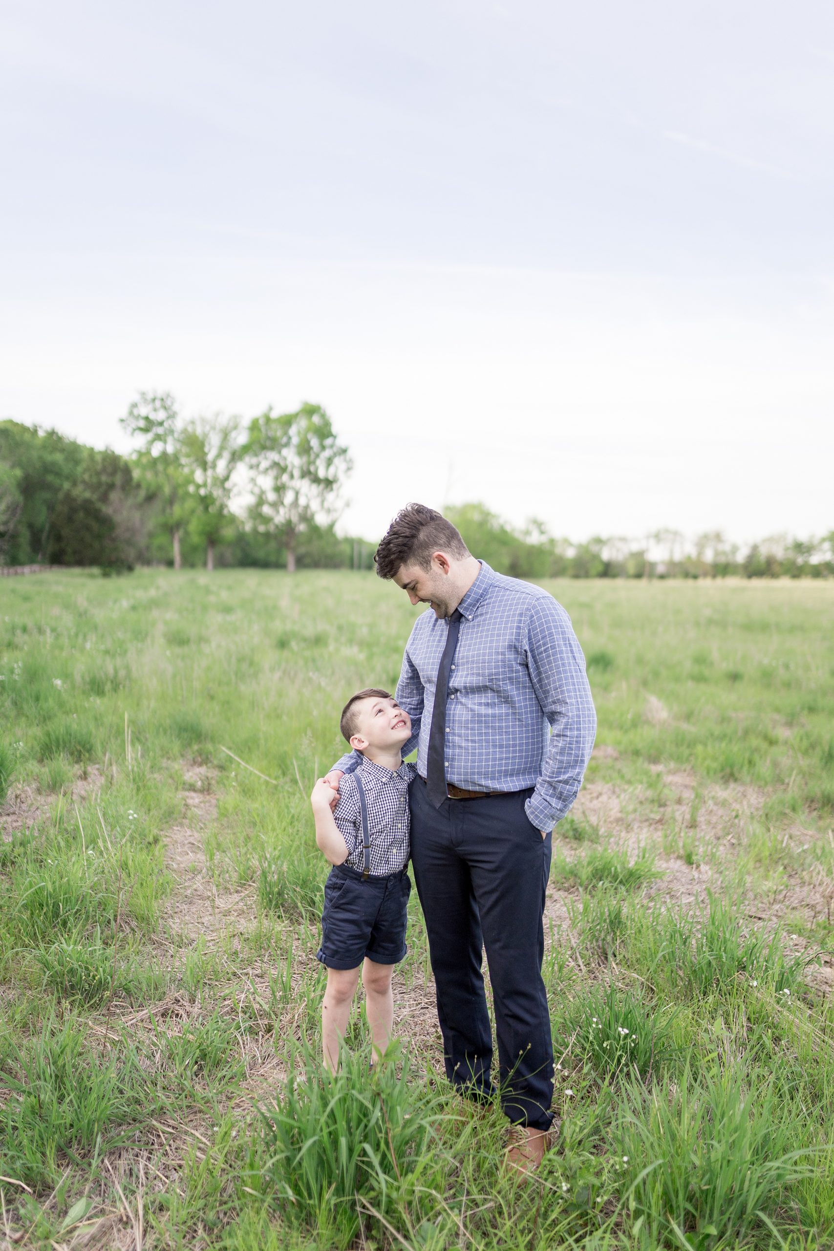dad and oldest son stand together looking at each other during family portraits