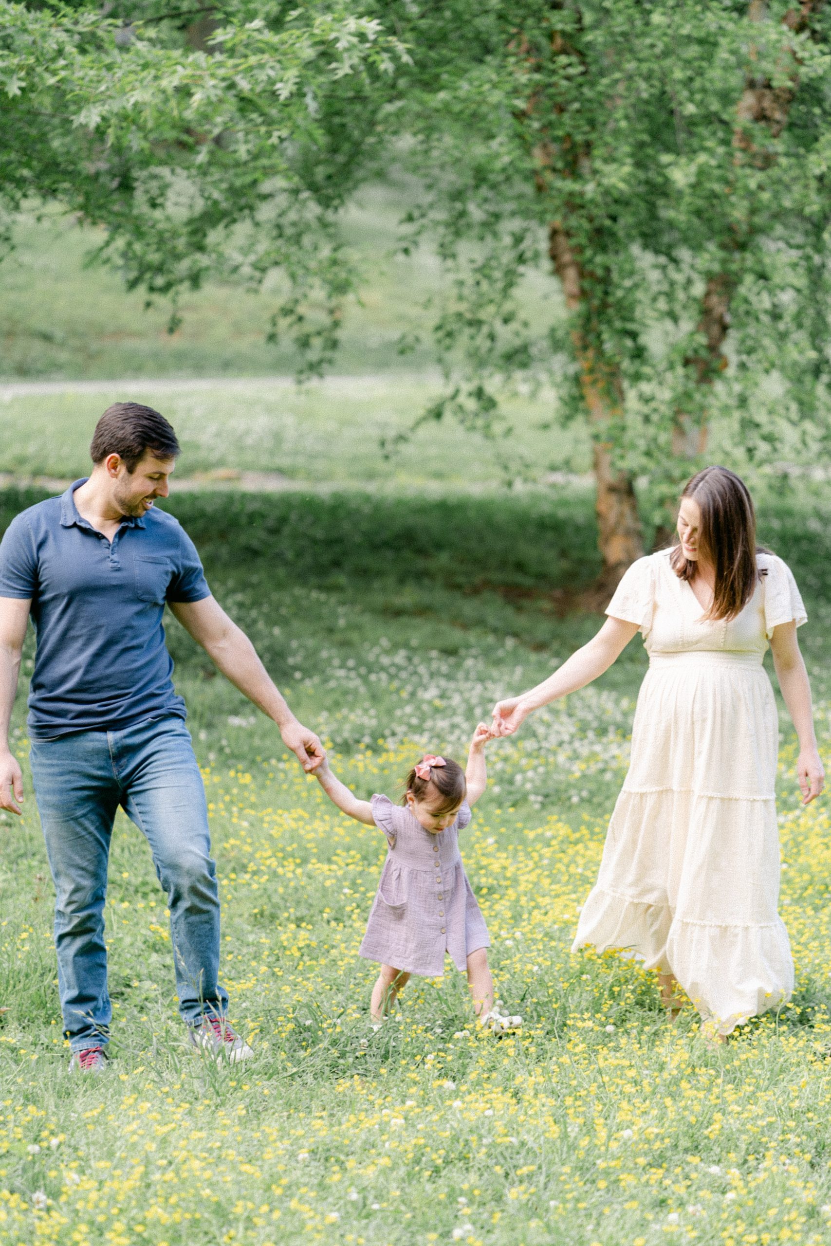 mom and dad hold hands with daughter in middle walking through field