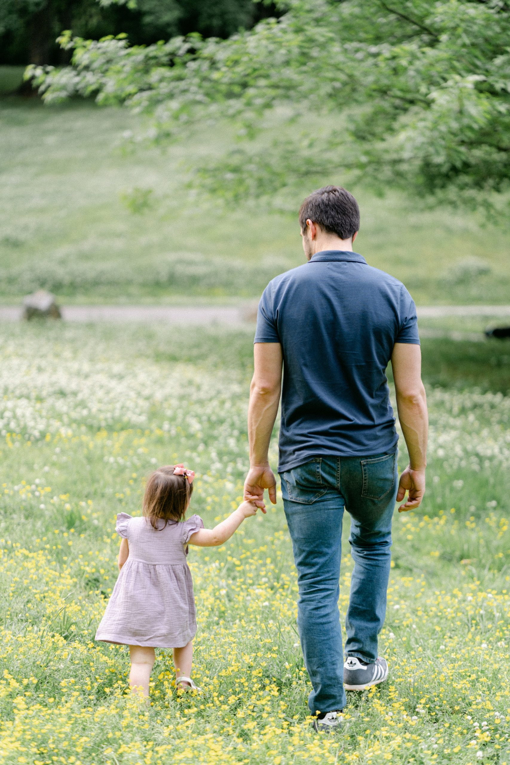 daddy and daughter hold hands and walk through field of flowers during Nashville family portraits