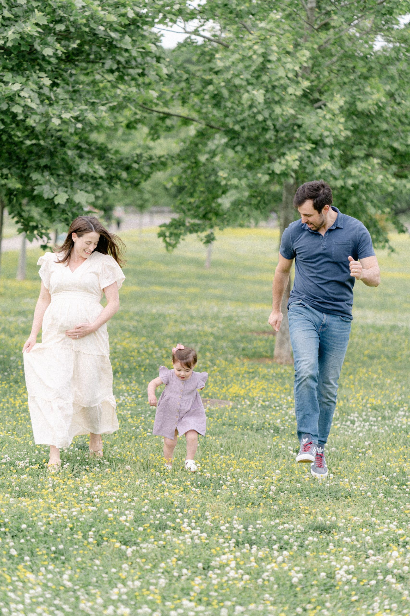 dad and pregnant mom run and play with toddler in field during Nashville photo session