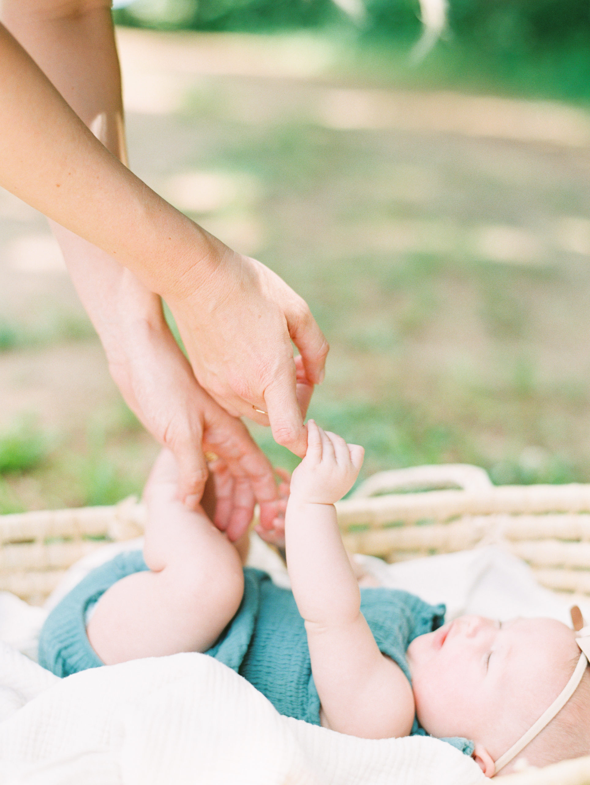 baby in woven basket holds mom's fingers