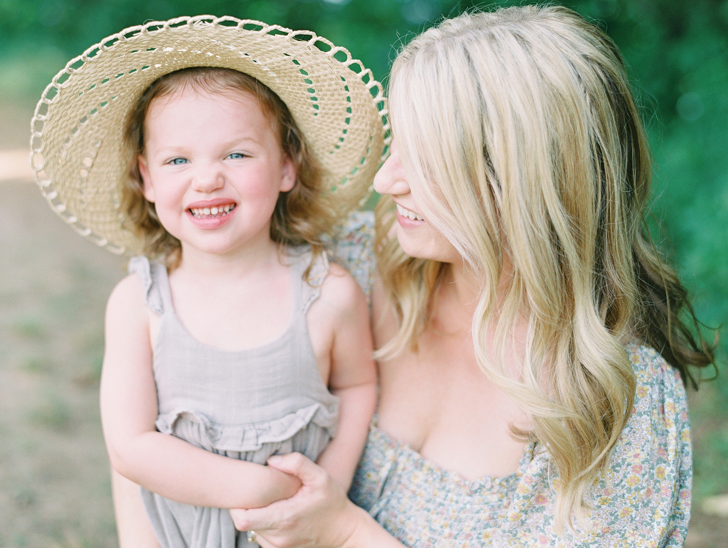 little girl smiles in hat while mom hugs her