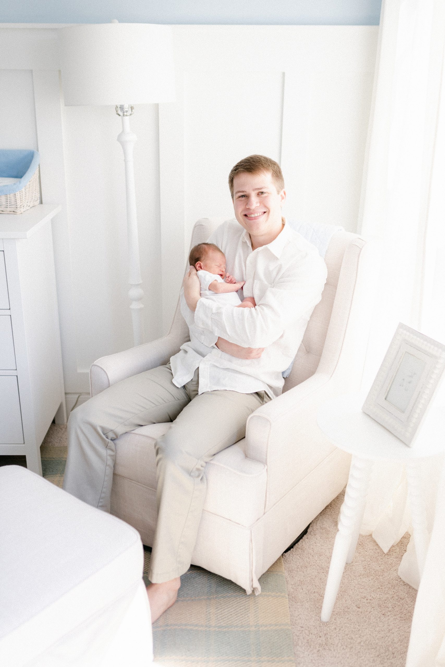 Murfreesboro dad holds newborn in nursery with side lighting during in-home newborn session