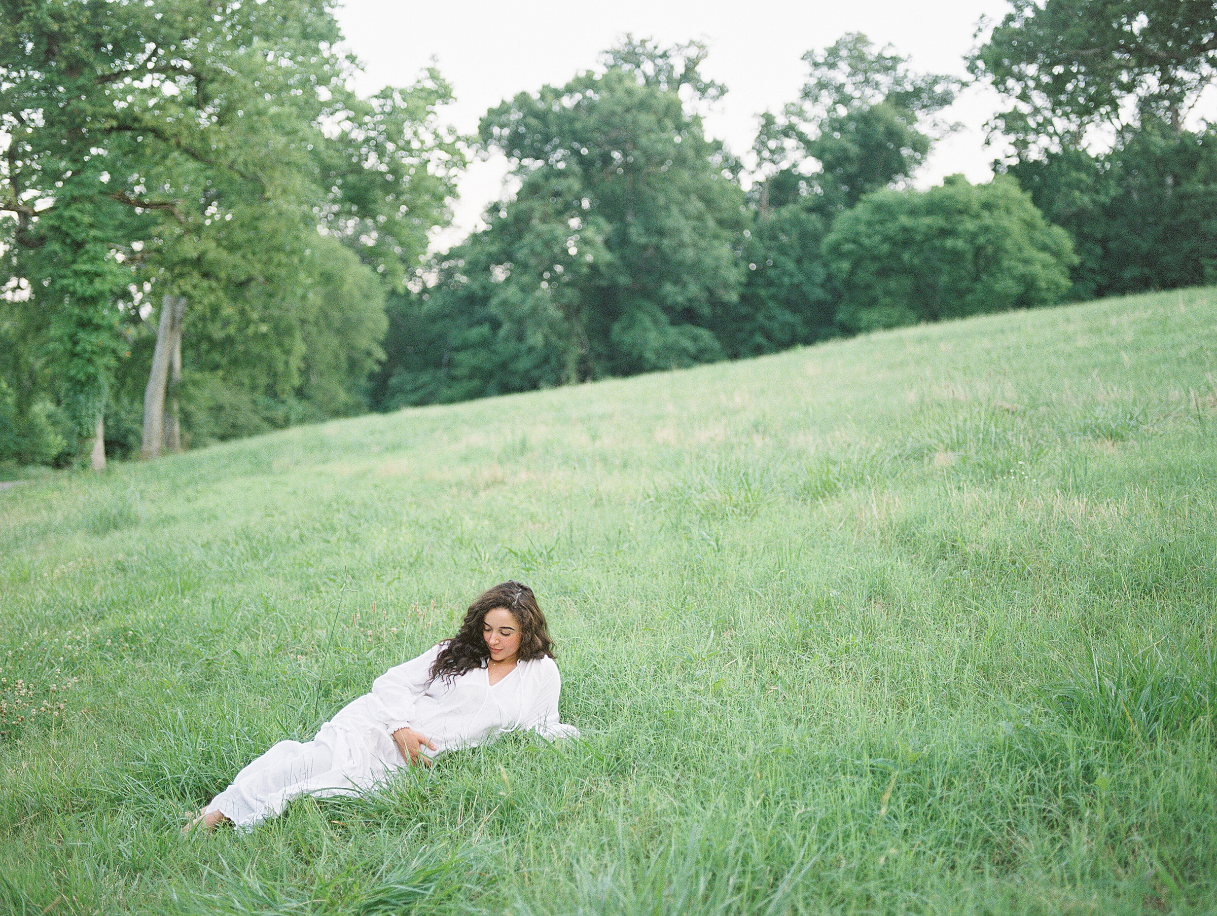 Woman lays on grassy hillside for Maternity Session in Nashville TN by Grace Paul Photography