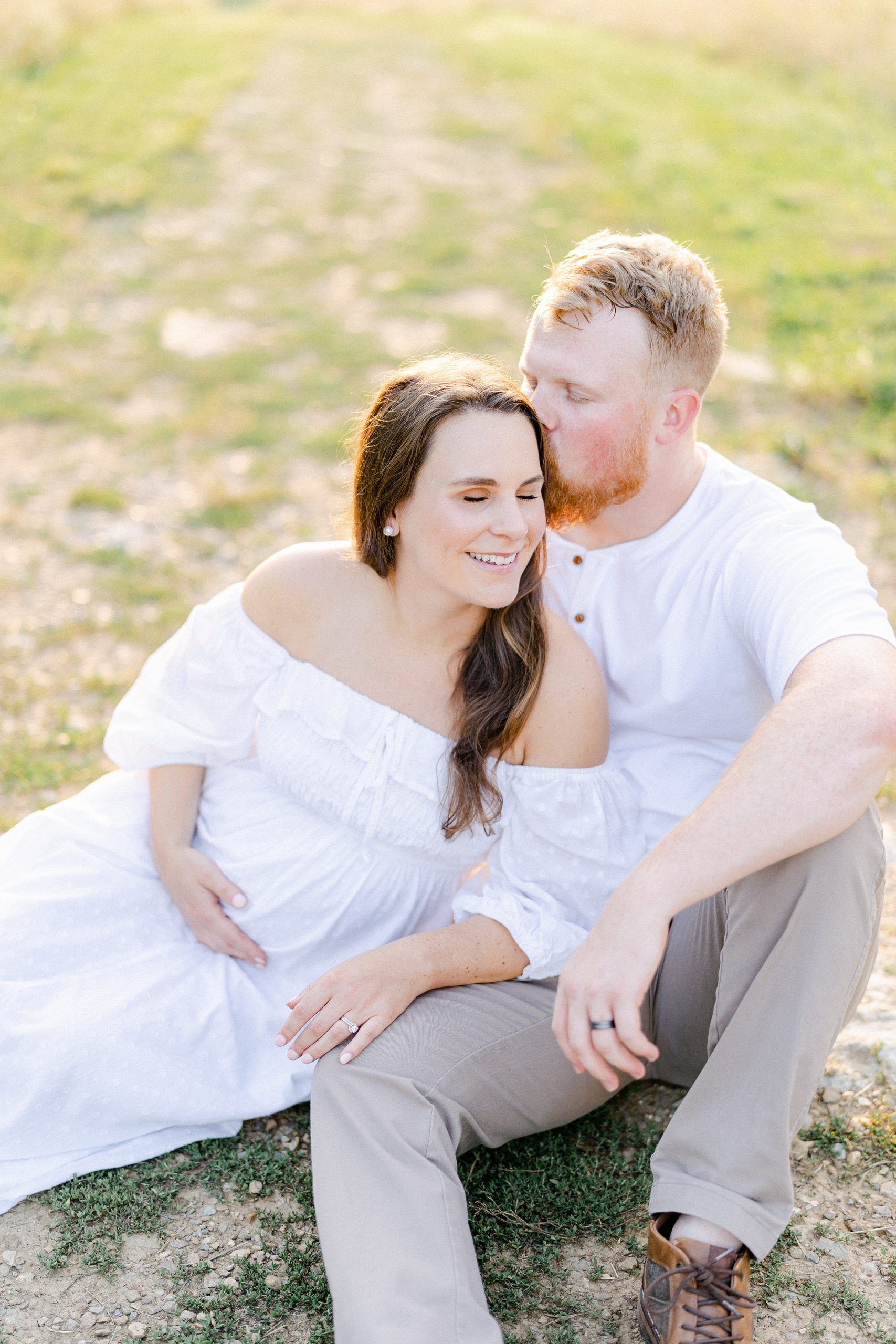 couple sits in grass and shares candid moment during maternity session