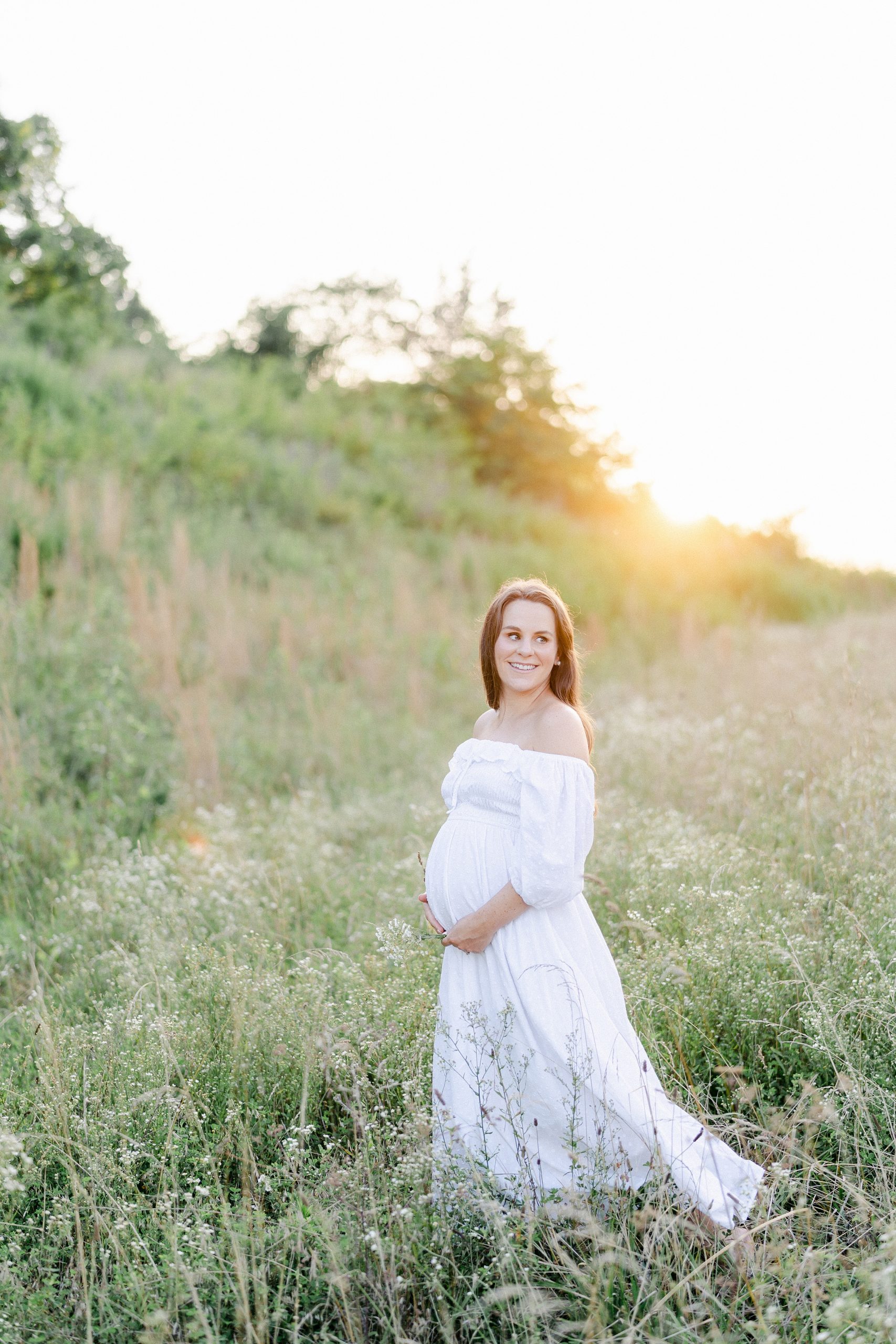 Pregnant mom stands in a field of tall grass and flowers during Brentwood TN Maternity Session by Grace Paul Photography