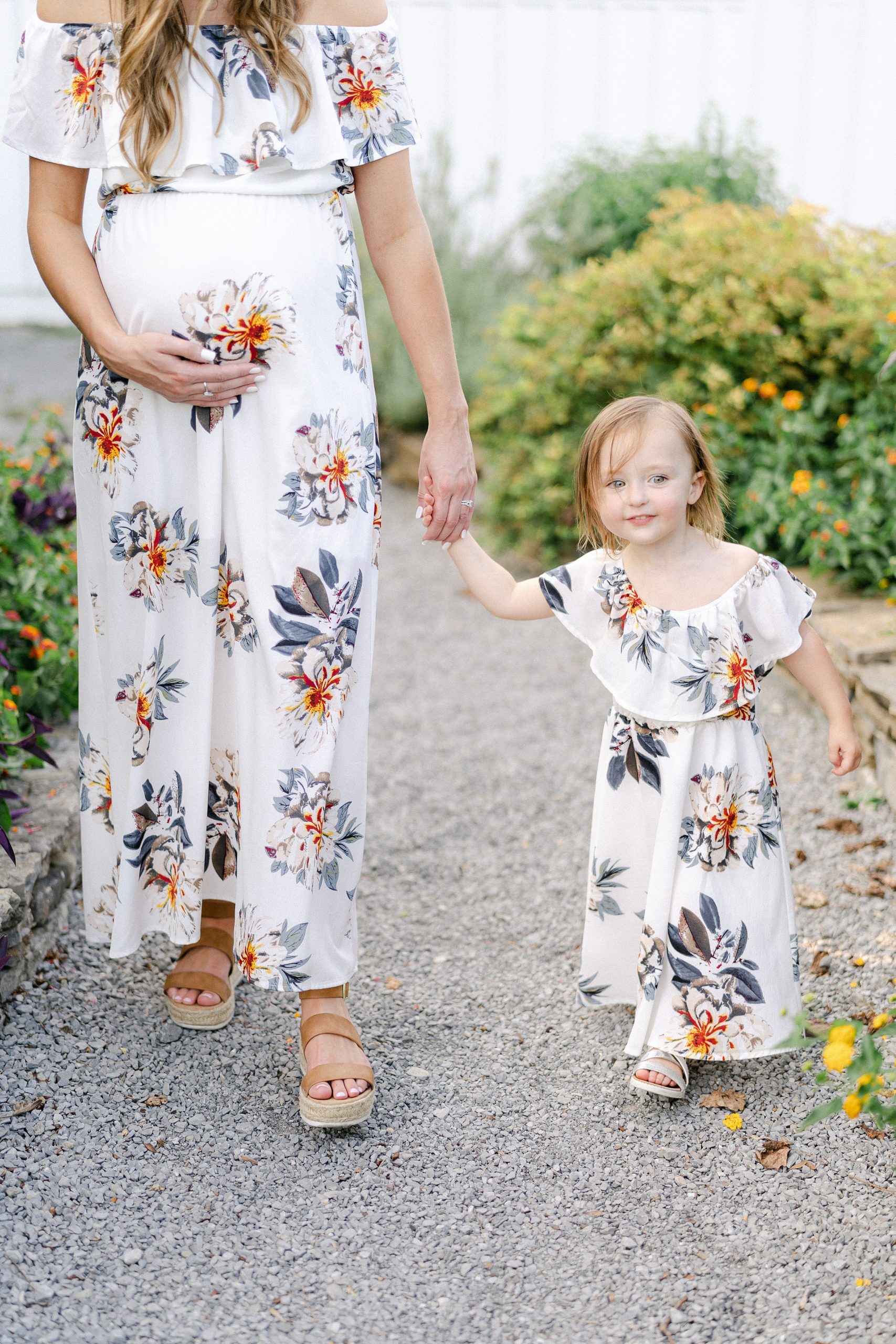 mom and little girl hold hands walking along gravel path during Mom + me session