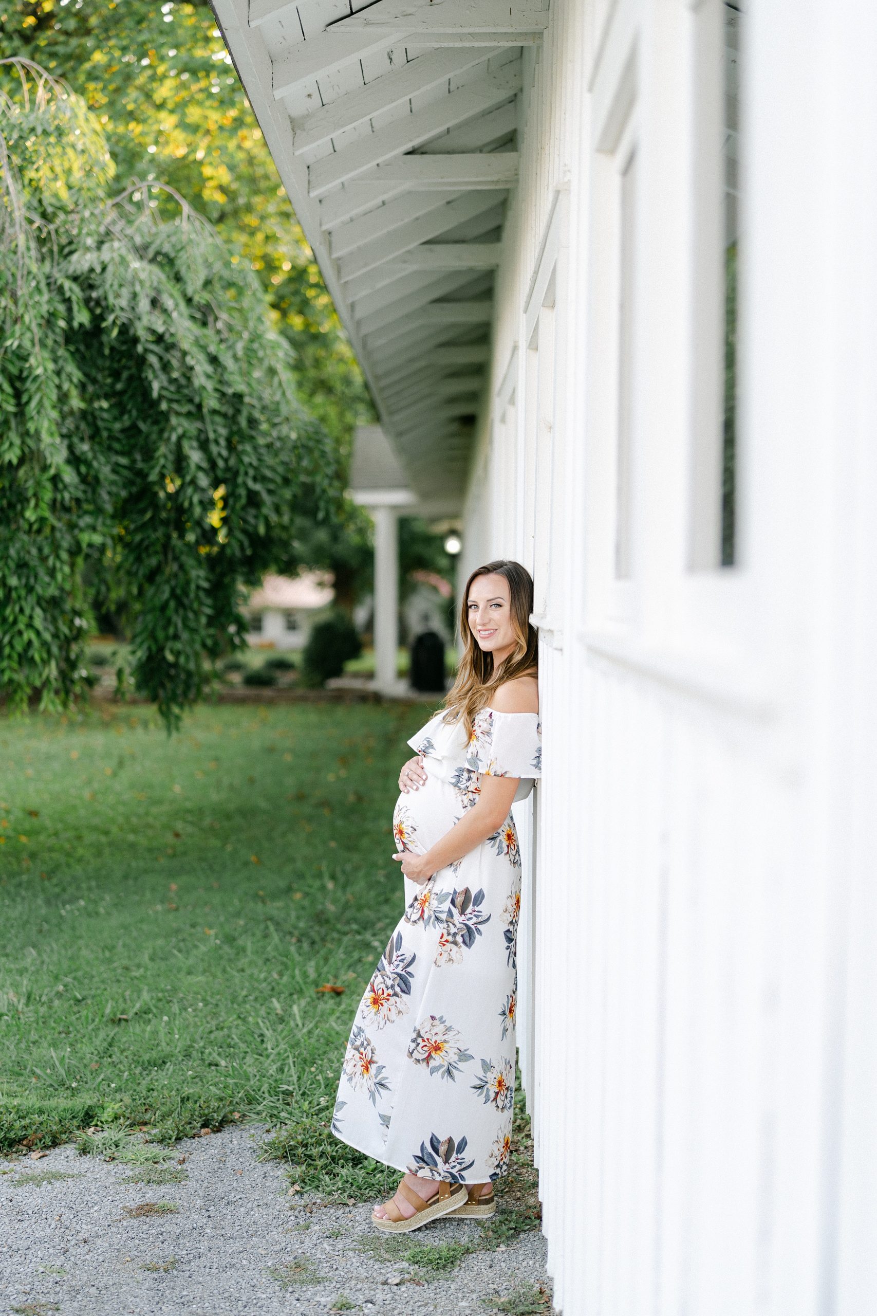 mom leans up against white building during maternity session in Nashville TN