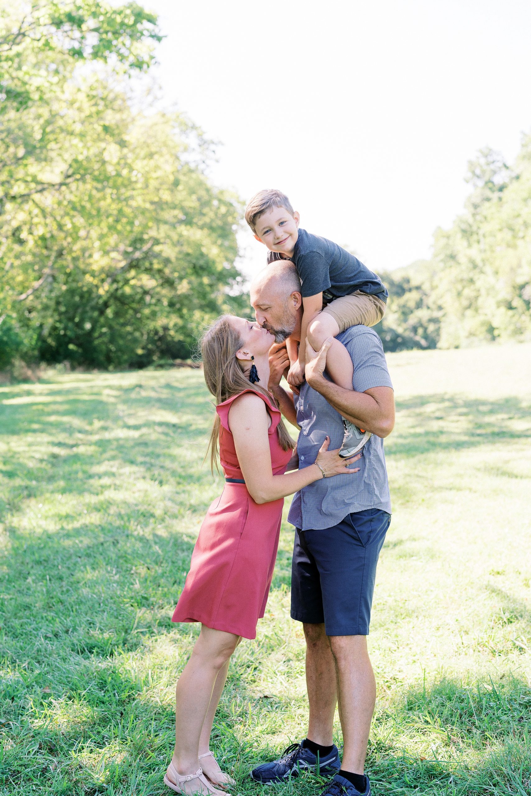 mom and dad kiss as dad holds son on his shoulders